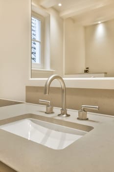 a bathroom sink with two faucets on the counter and an open window in the wall is behind it