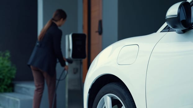 A woman unplugs the electric vehicle's charger at his residence. Concept of the use of electric vehicles in a progressive lifestyle contributes to a clean and healthy environment.