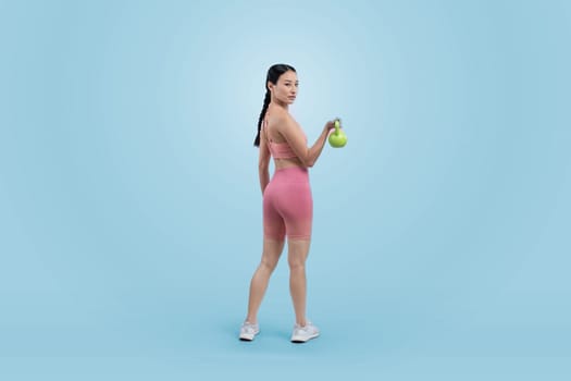 Vigorous energetic woman doing kettlebell weight lifting exercise on isolated background. Young athletic asian woman strength and endurance training session as body workout routine.