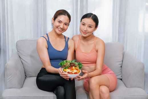 Young sporty Asian women in sportswear holding salad bowl together fill with vibrant of fruit and vegetable. Natural youthful and fit body lifestyle with balance nutrition and home exercise. Vigorous