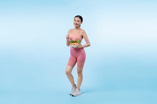 Young sporty Asian woman in sportswear holding salad bowl fill with vibrant of fruit and vegetable. Natural youthful and fit body lifestyle with balance nutrition on isolated background. Vigorous