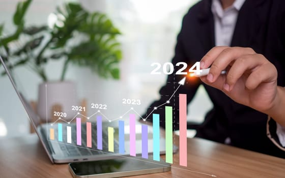 Stock trading. Finance. Investing. Growing business. Businesswoman in suit pointing with a pen at the tip of an arrow and a graph bar Represents business growth in 2024. concept of goals for 2024