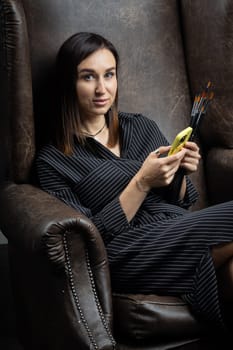 a young brunette female artist stands behind an easel. photo shoot on a black background in the studio