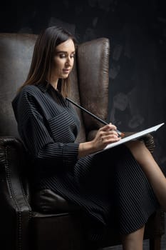 a young brunette female artist stands behind an easel. photo shoot on a black background in the studio