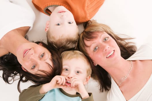 two adult sisters with their sons lie on their backs and look at the camera