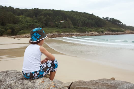 Boy sitting on the stone from the beach