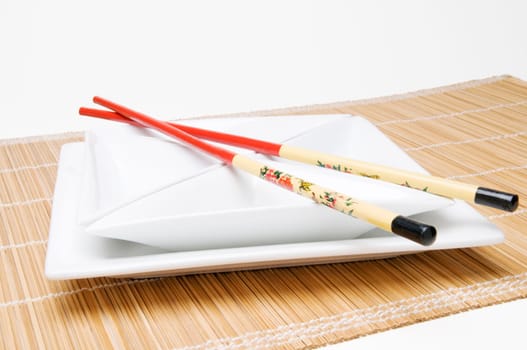 white,square bowl set with chopsticks on top on bamboo base