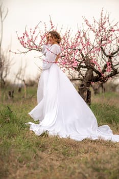 Woman peach blossom. Happy curly woman in white dress walking in the garden of blossoming peach trees in spring.