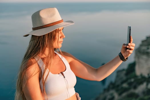 Selfie woman in hat, white tank top and shorts makes selfie shot mobile phone post photo social network outdoors on sea background beach people vacation lifestyle travel concept