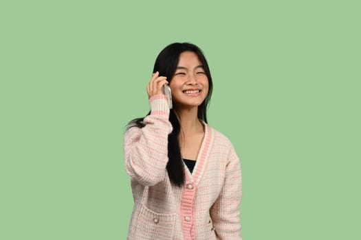 Portrait of a smiling teenage asian girl talking on mobile phone isolated over green background.