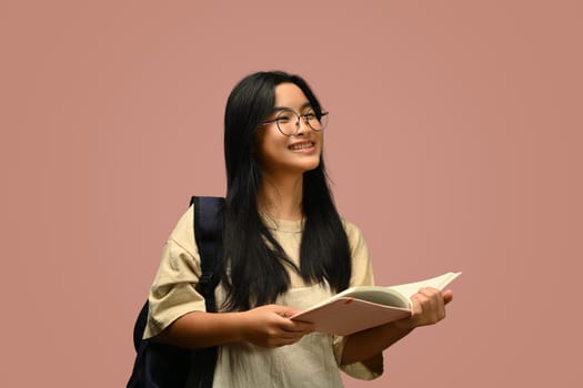Teenager schoolgirl wearing glasses holding textbook over pink background. Educational, learning and back to school concept..