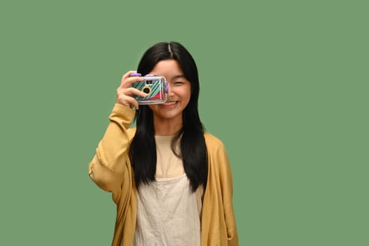 Happy Asian teenage girl with film camera posing isolated on green background.