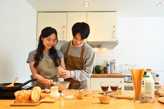 Loving couple having fun while preparing food, making pancakes in cozy kitchen at home.