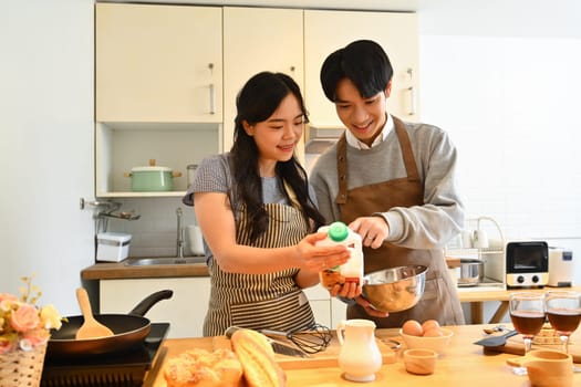 Loving young couple preparing dough for making fresh breakfast pancakes in kitchen..