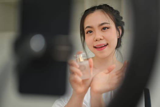 Asian woman beauty blogger showing perfumes to camera while making new video for her beauty channel..
