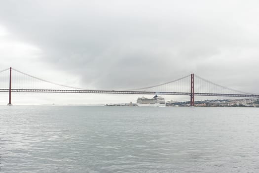 A cruise ship passes along the river under the bridge in cloudy weather. Mid shot