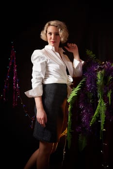 An elegant blonde girl in white blouse in a room decorated for Christmas or new year with a background, tinsel and light garlands
