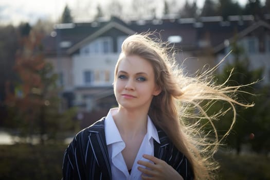 Portrait of Beautiful girl with long blonde hair in white shirt and jacket in village or small town. High young slender woman in an autumn, spring, summer day