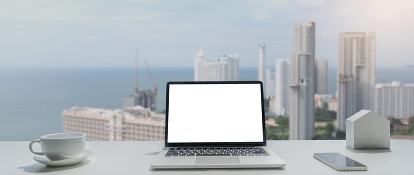 Image of working space by the window equipment in office interior, open laptop computer with mock up screen.