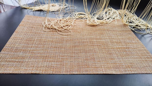 Brown or beige woven napkin, similar to burlap on a black surface. Background, texture, frame and copy space. Concept of beautiful decor and comfort in the house