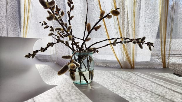 A bouquet made of willow branches on table near the window with curtains and daylight sun. The concept of spring. Preparation for the religious holiday of Easter