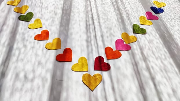 Multicolored hearts made of rough velvet paper on white surface with stripes of shadow and light from the sun. Abstract background, texture, copy space