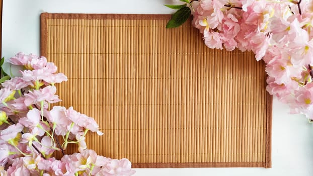 Branch with pink cherry blossom flowers on white background and bamboo napkin or mat. Texture, frame, copy space, background