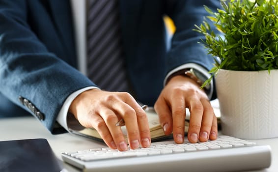 Male arms in suit typing on silver keyboard using computer pc at office workplace closeup. Accountant finger job modern lifestyle web search assistant enter account login password and note credential