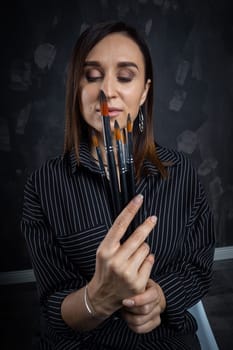 Portrait of a female artist, with brushes in her hands.
 Photo shoot on a black background in the studio