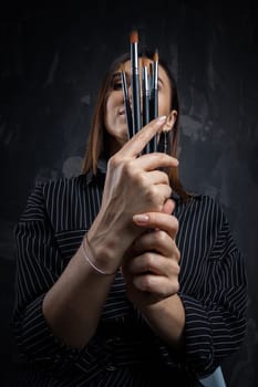 Portrait of a female artist, with brushes in her hands.
 Photo shoot on a black background in the studio