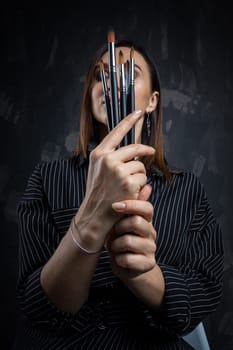 Portrait of a female artist, with brushes in her hands.
 Photo shoot on a black background in the studio