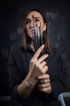 Portrait of a female artist, with brushes in her hands.
 Photo shoot on a black background in the studio