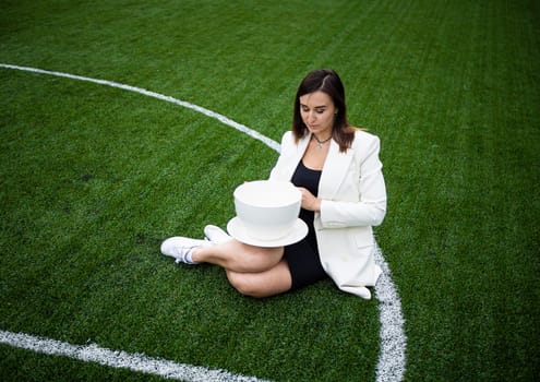 A business woman with a large cup, sitting on a green lawn in the park. The concept of an office worker on a picnic.