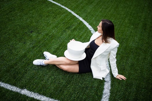 A business woman with a large cup, sitting on a green lawn in the park. The concept of an office worker on a picnic.