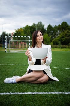 A business woman with a large cup, sitting on a green lawn in the park. The concept of an office worker on a picnic.