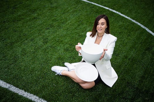 A business woman with a large cup, sitting on a green lawn in the park. The concept of an office worker on a picnic.