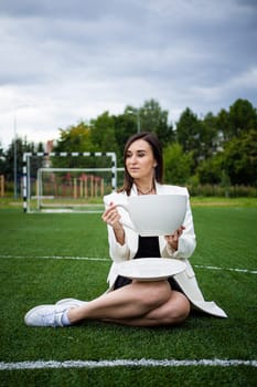 A business woman with a large cup, sitting on a green lawn in the park. The concept of an office worker on a picnic.