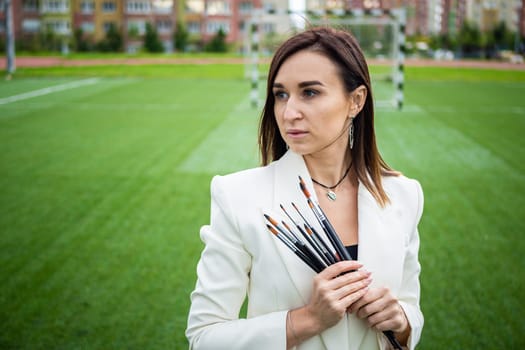 Brunette, female artist paints in nature. She has paint brushes in her hands.