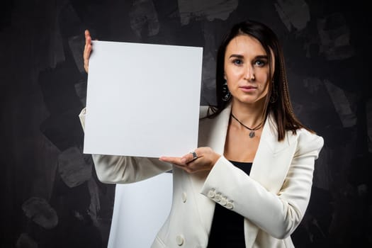 A business woman holds an empty sign in front of the camera. Shot in the studio on a dark background.