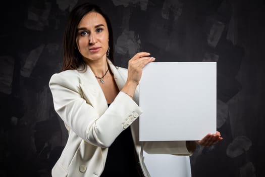 A business woman holds an empty sign in front of the camera. Shot in the studio on a dark background.