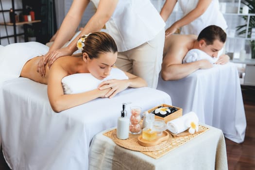 Caucasian couple customer enjoying relaxing anti-stress spa massage and pampering with beauty skin recreation leisure in day light ambient salon spa at luxury resort or hotel. Quiescent