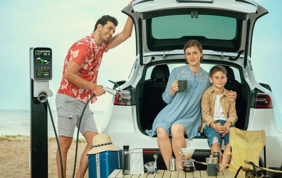 Family vacation trip traveling by the beach with electric car, happy family recharge EV car, enjoying outdoor camping coffee. Seascape travel and eco-friendly car for clean environment. Perpetual