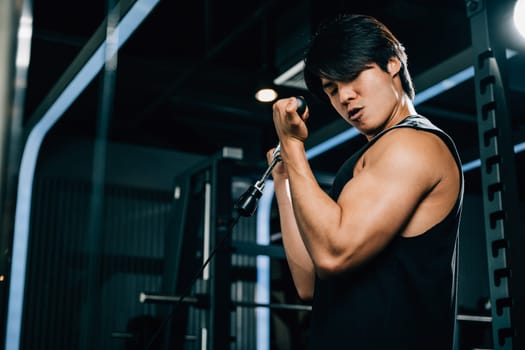 A slim and toned Asian person performing cable triceps pull up, using the gym equipment to shape their body and build muscle. lifestyle and people concept