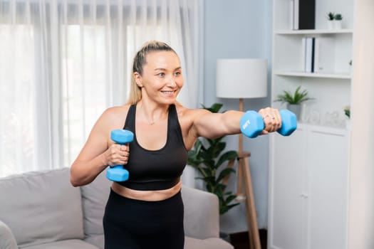 Athletic and sporty senior woman engaging in body workout routine with lifting dumbbell at home as concept of healthy fit body with body weight lifestyle after retirement. Clout