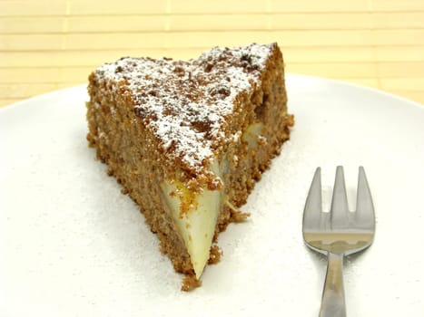 A piece of pear cake on a white plate dusted with powdered sugar