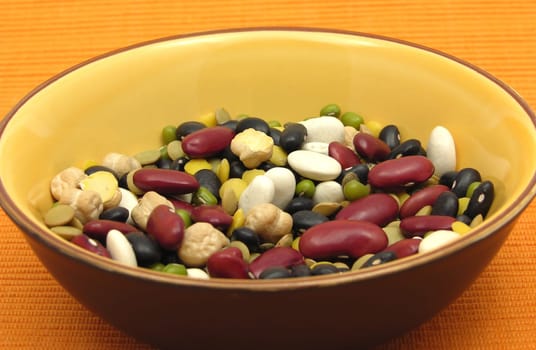 Mixed colorful legumes in ceramic bowl on orange background