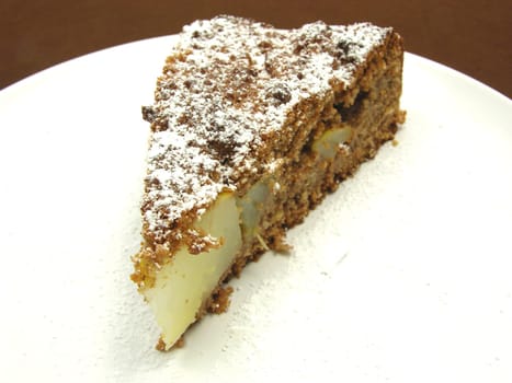 A piece of pear cake on a white plate dusted with powdered sugar
