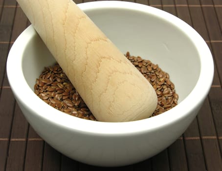 Flaxseed in porcelain bowl with mortar on placemat
