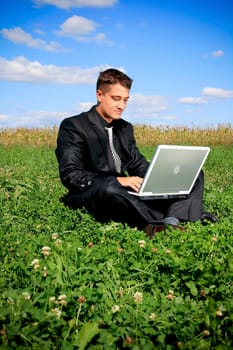 Businessman in the middle of the field on laptop