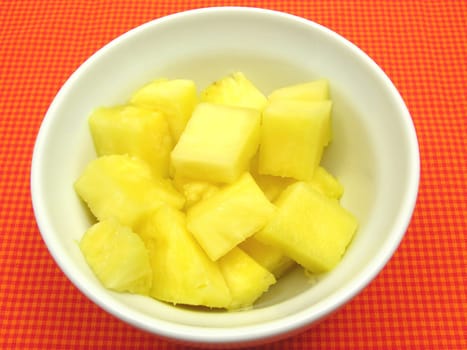 Pineapple pieces in a white porcelain bowl on a red-checkered base